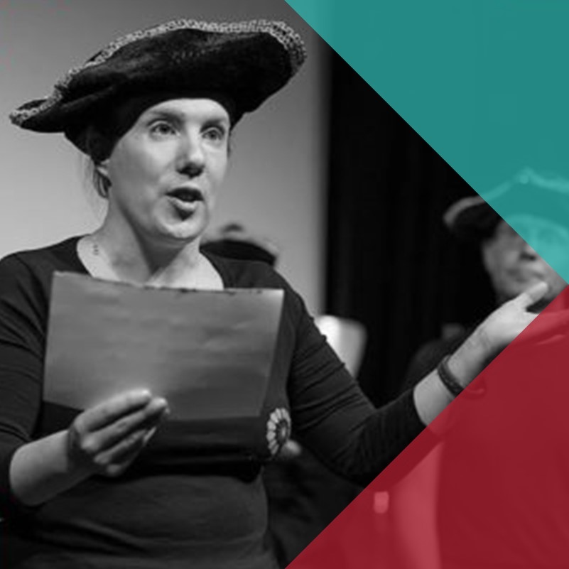 A black and white photo of a woman in costume delivering a speech on stage with a man in costume in the background